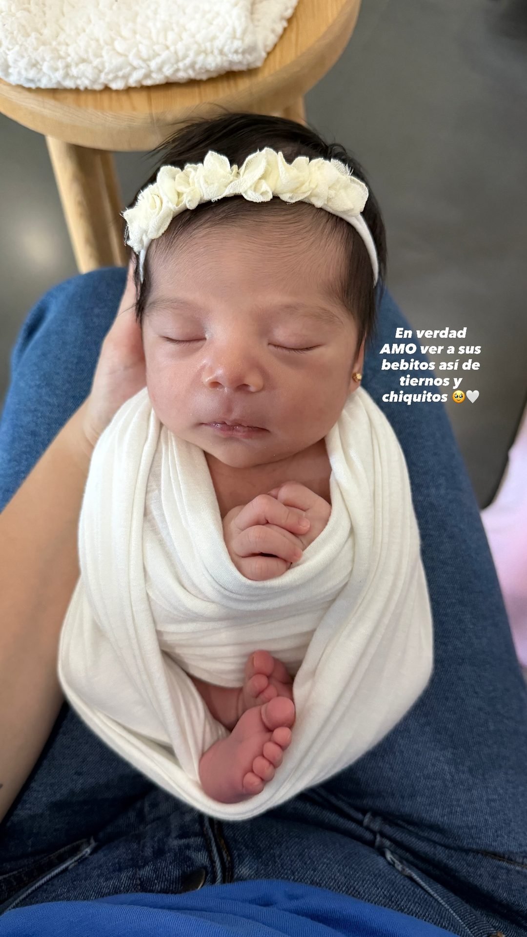 Bebé envuelta en blanco con diadema de flores, cargada por su mamá