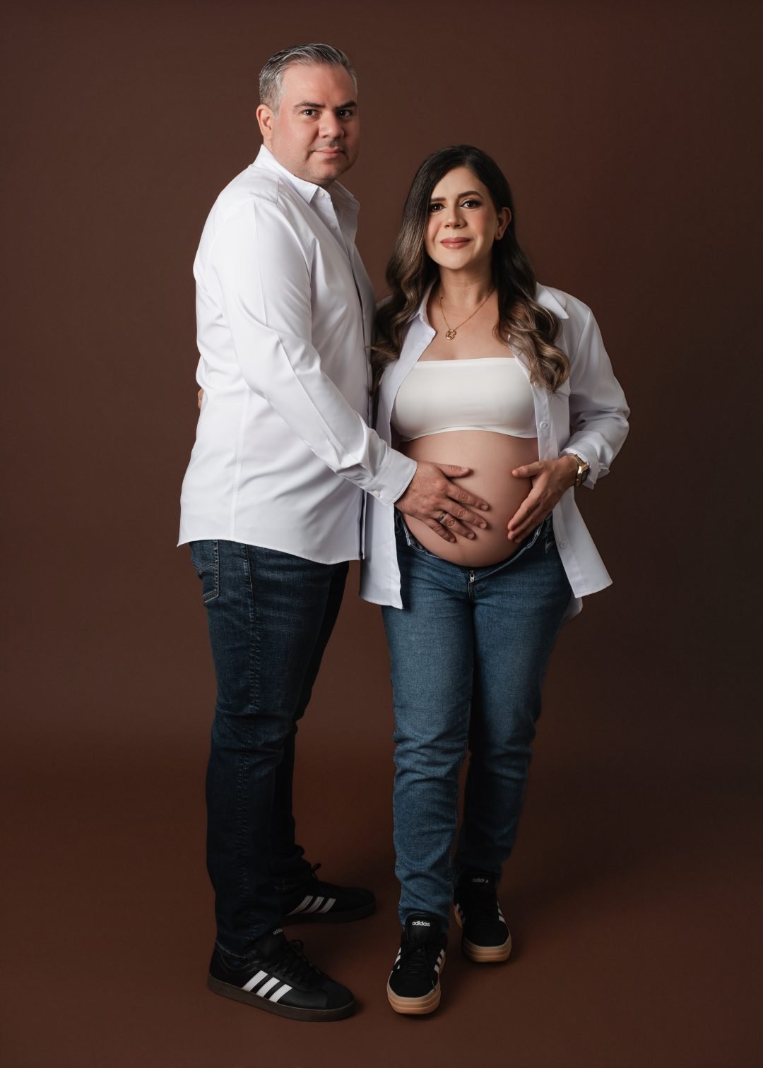 pareja embarazada abrazándose de cerca vestidos de blanco