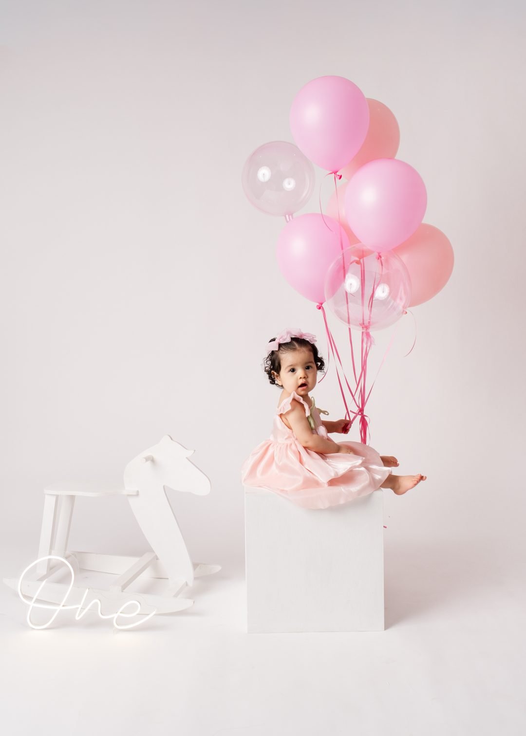 niña posando sola junto a globos rosas de su cumpleaños