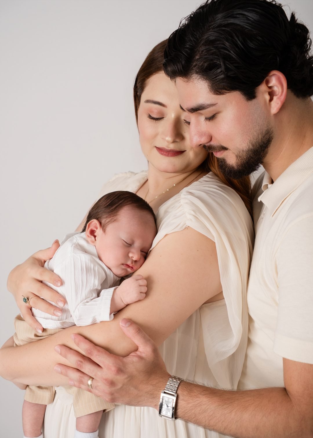 papás abrazando a su bebé recién nacido en tonos crema